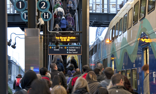 An almost full platform at King Street Station while people deboard the train. People all funnel up the stairs to connect to other transit stops and their final destinations.